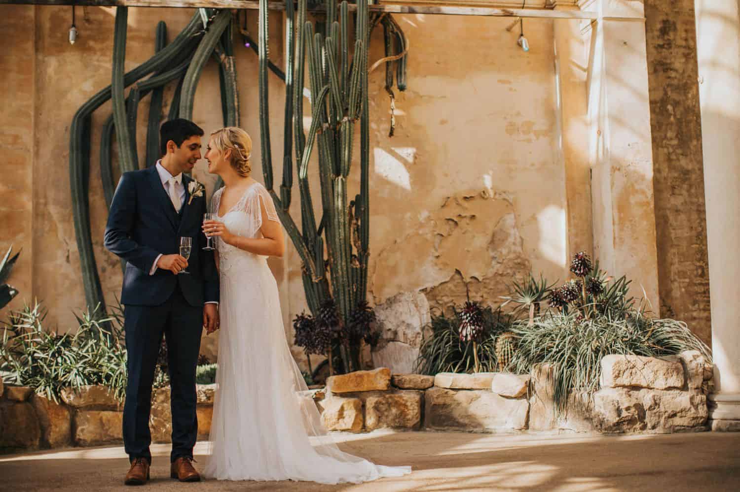 How To Make A Photography Website Your Dream Clients Can’t Resist: A bride and groom stand face-to-face, holding champagne in an adobe setting.